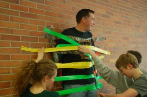 Students pitch in to tape math teacher Jason Gehoski to the cafeteria wall during lunch.