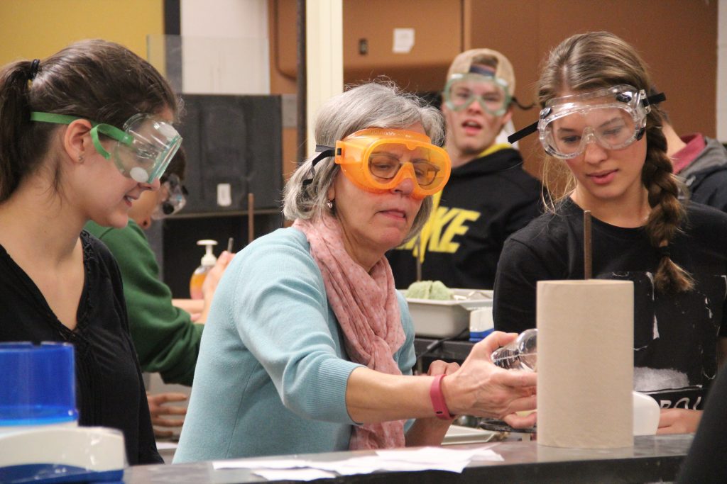 Safety First: Science teacher Mary Fredell concentrates as she helps juniors Hailey Laplow and Chassadee Winters in Chemistry students out with completing their lab. Safety is one of the main priorities in the lab to prevent dangerous mistakes from happening. All of the students are required to wear goggles and aprons in the lab. Photo by Eline Ferket